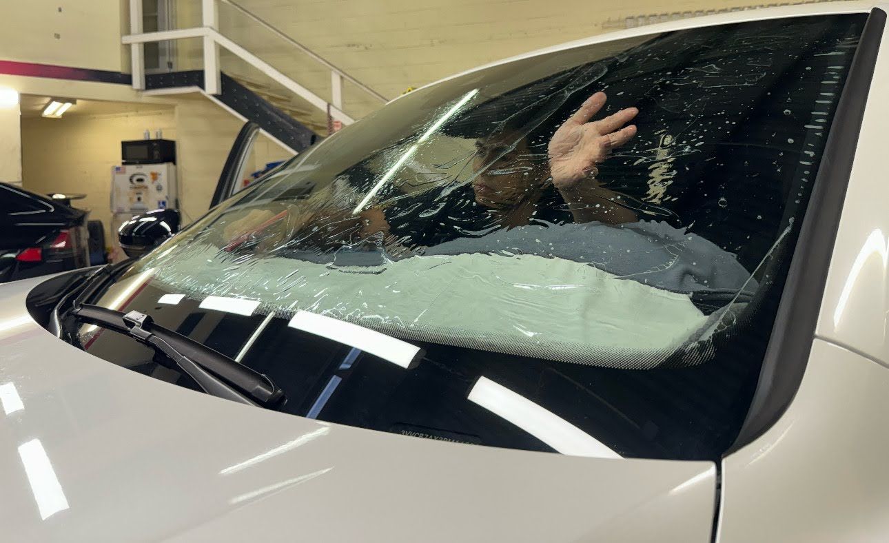 Person inside a white car with a shattered windshield in a parking garage