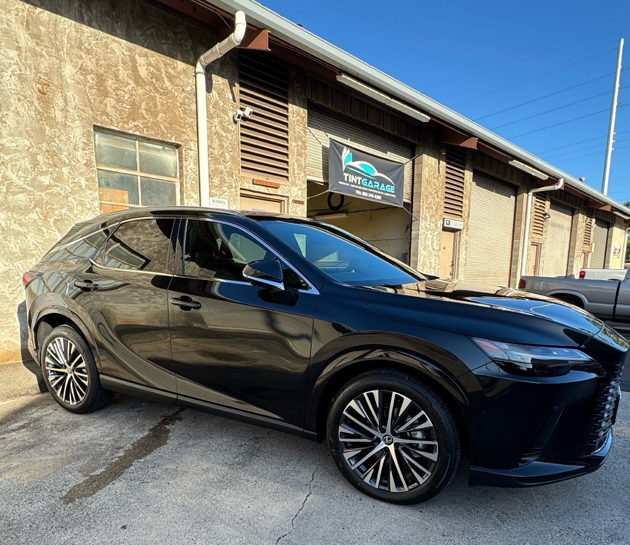 Black SUV parked beside a weathered building in bright sunlight.
