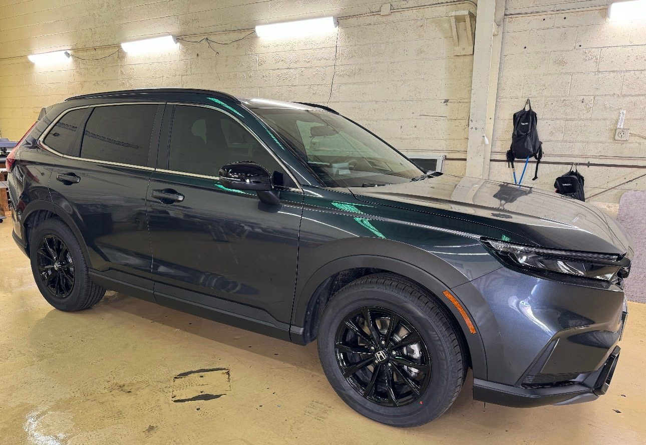 Black SUV parked indoors in a garage, side view with black wheels and gray front bumper