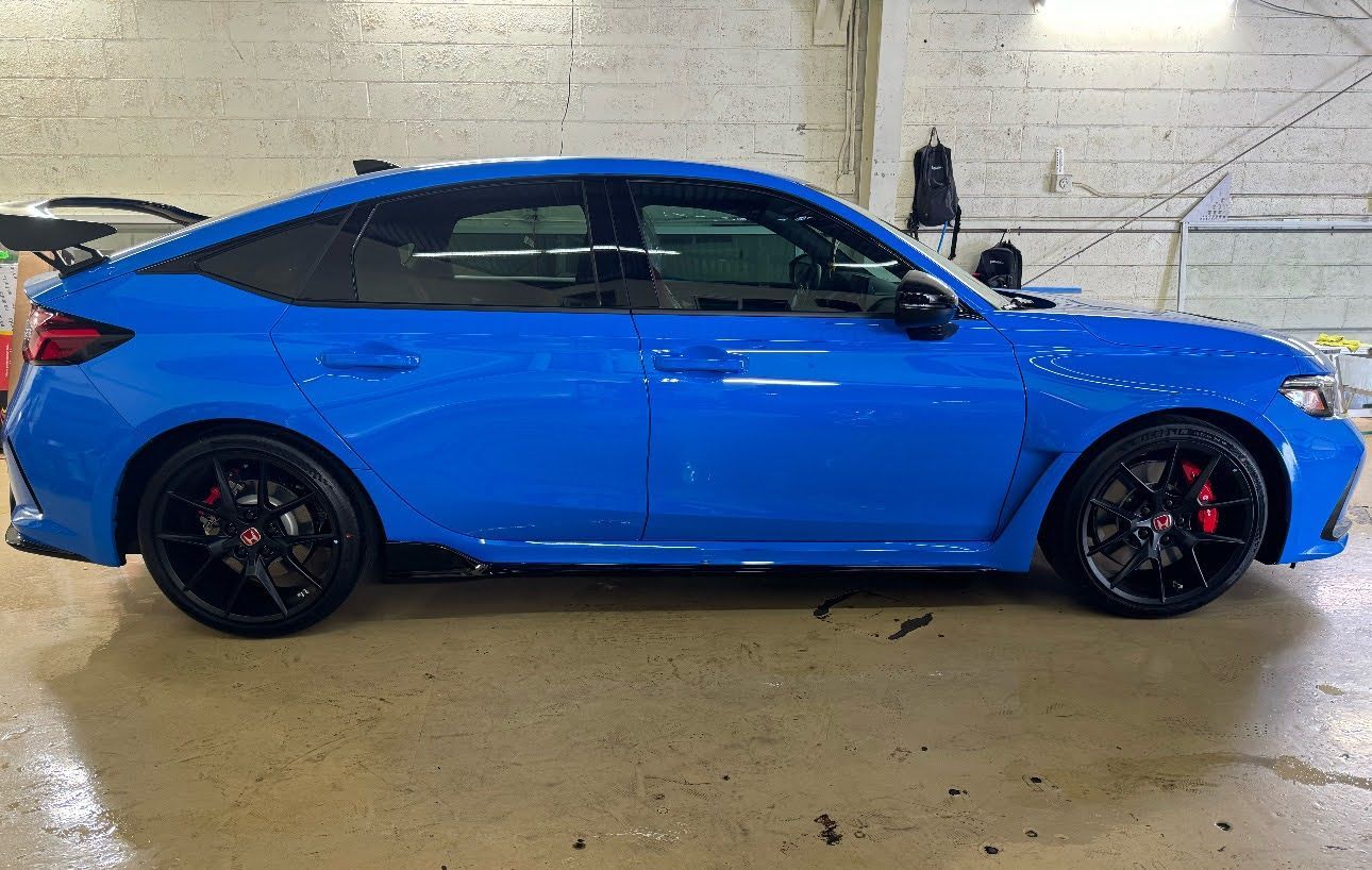 Blue sports sedan parked indoors on a wet concrete floor, side view.