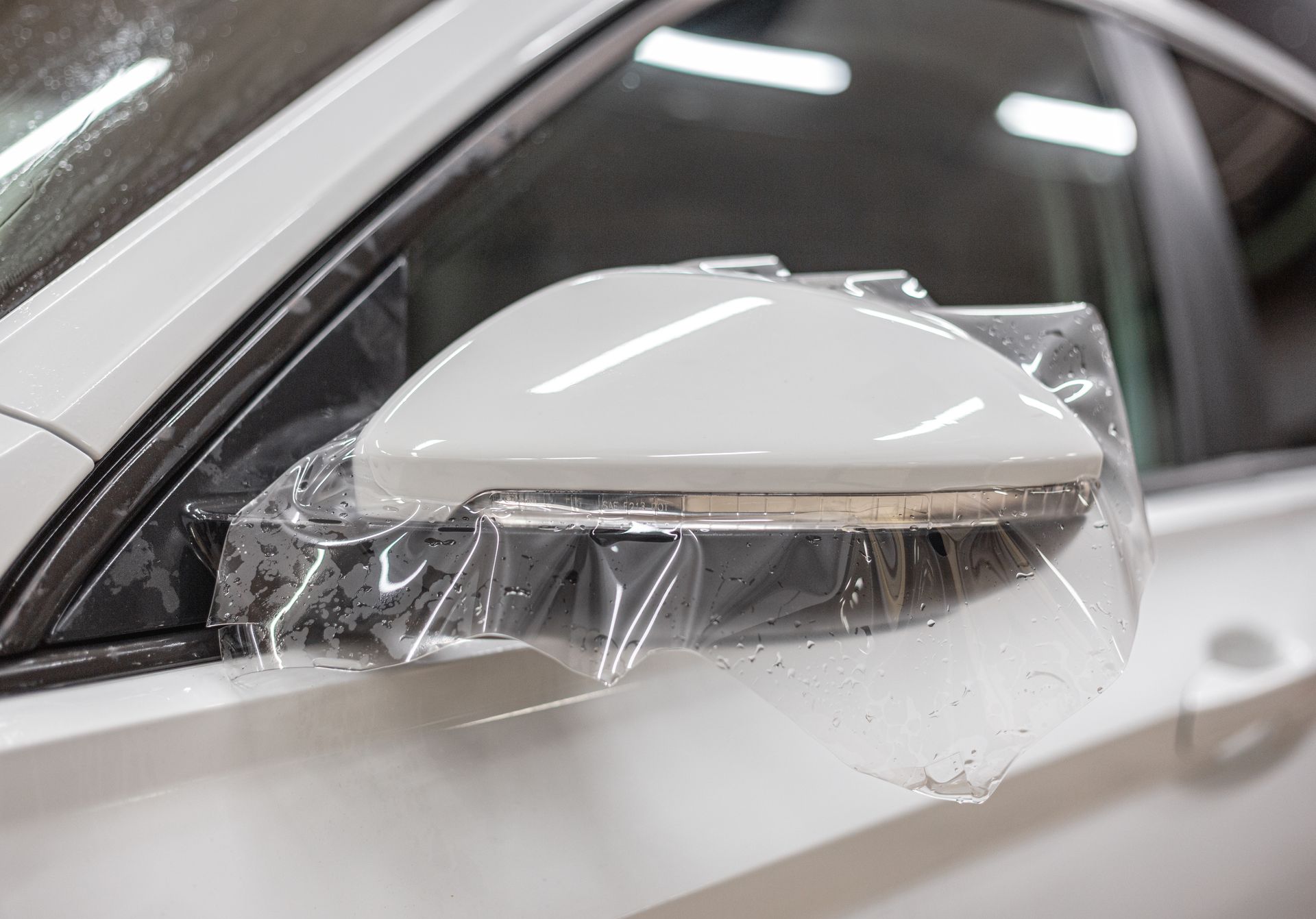 White car side mirror wrapped in clear protective plastic film