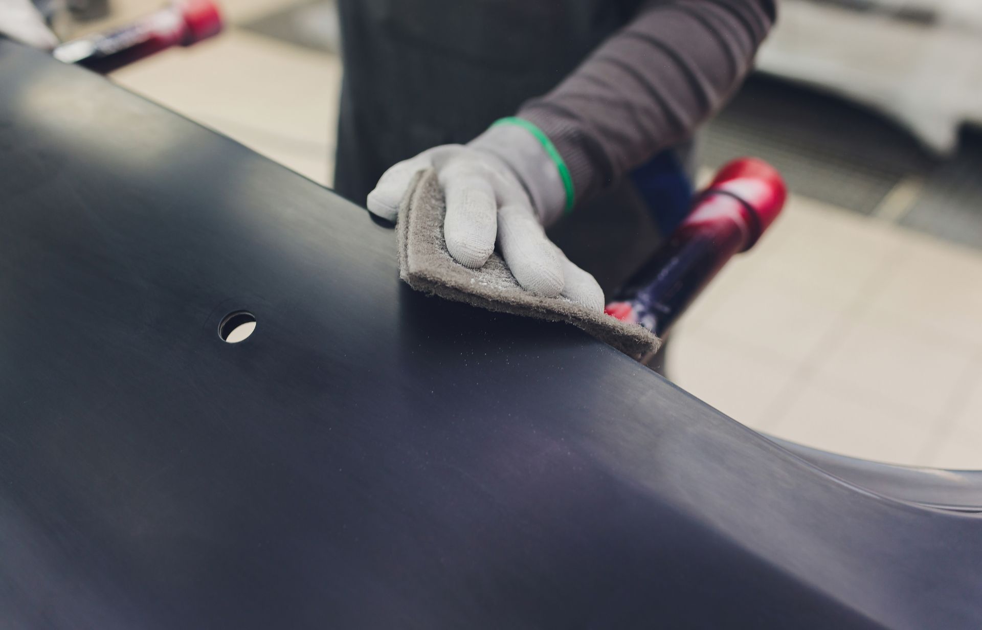 Gloved hand smoothing black material with a tool on a work surface