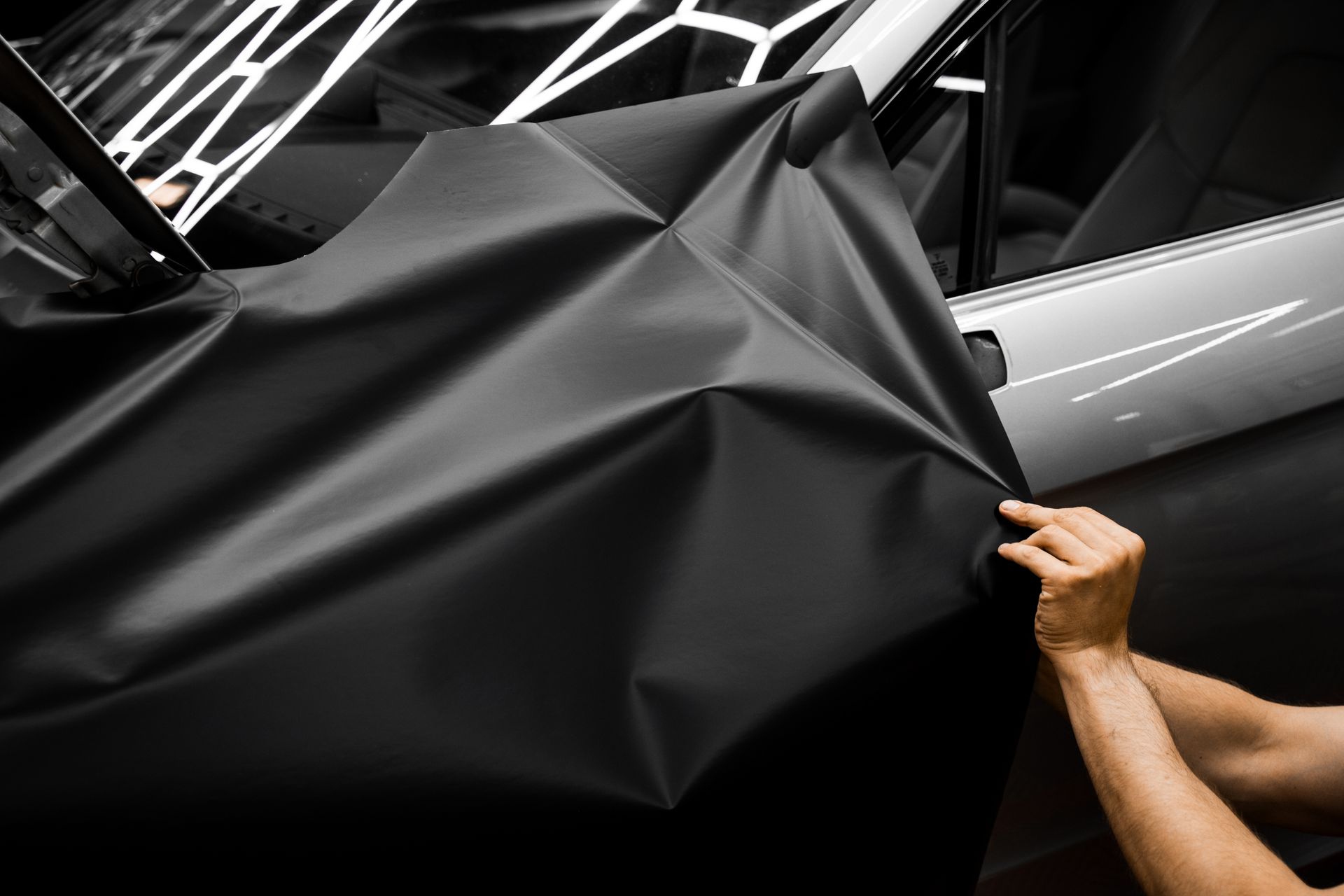 Hands pulling a black cover off a sleek gray car in a showroom