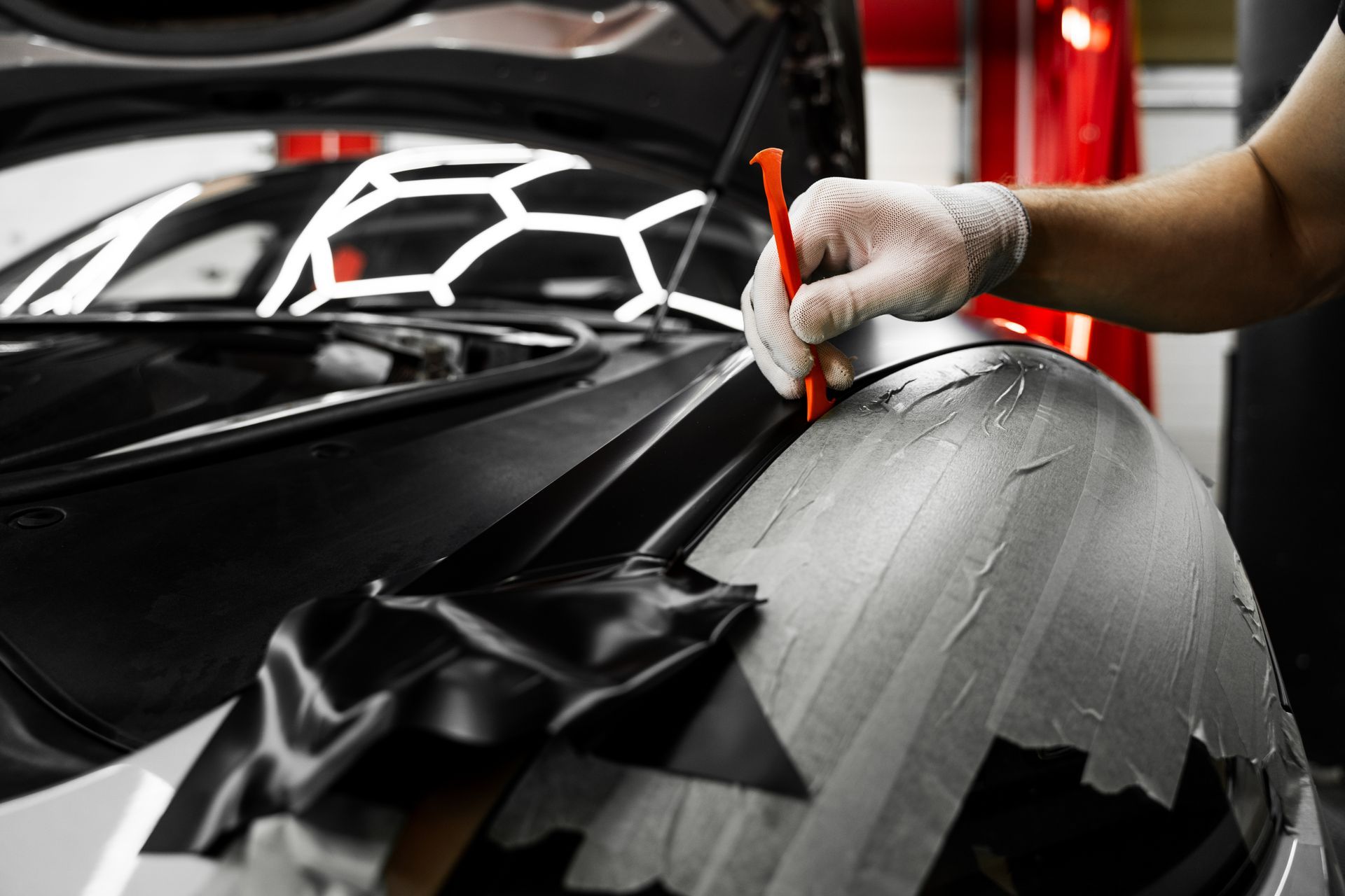 Gloved hand polishing a black car’s hood with a red cloth in a garage