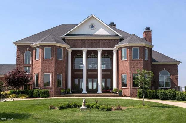 Red brick mansion with white columns and black roof, set on a green lawn under a blue sky.