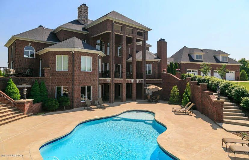 Large brick house with pool, patio, and detached garage on a sunny day.