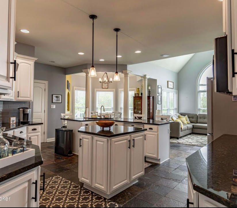 Spacious white kitchen with dark countertops, two islands, open to dining area and living room with gray walls.