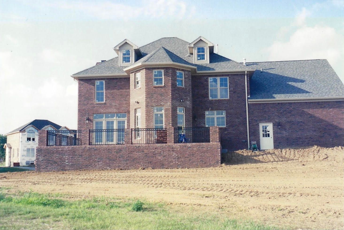 Red brick house with retaining wall, side door, and three dormers. Construction site setting.