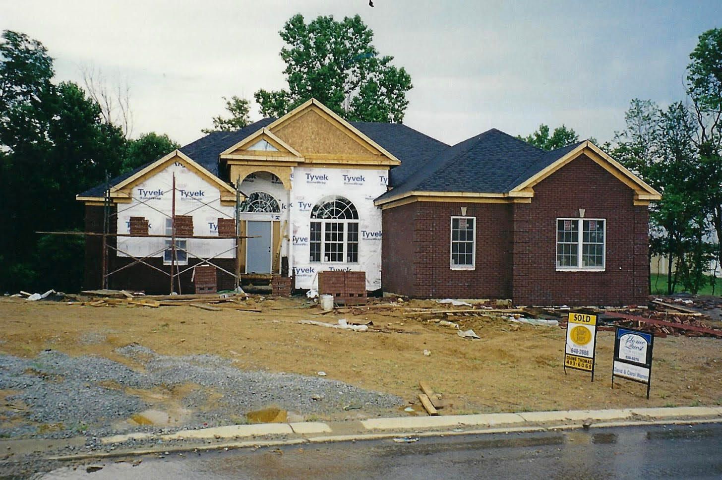 House under construction, red brick exterior, roof nearing completion, overcast day.