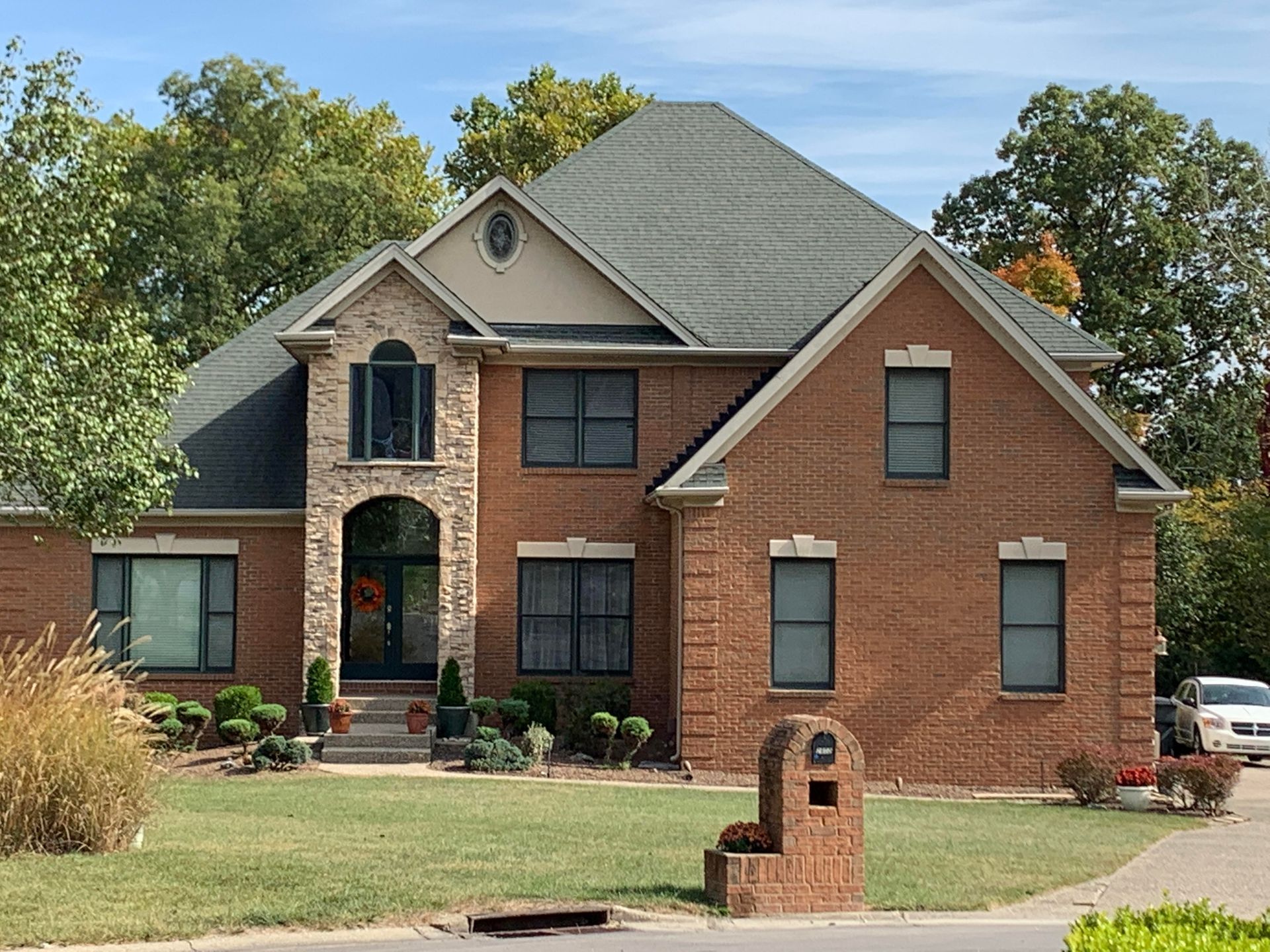 Two-story brick house with green roof, arched entry, and mailbox on a grassy lawn.