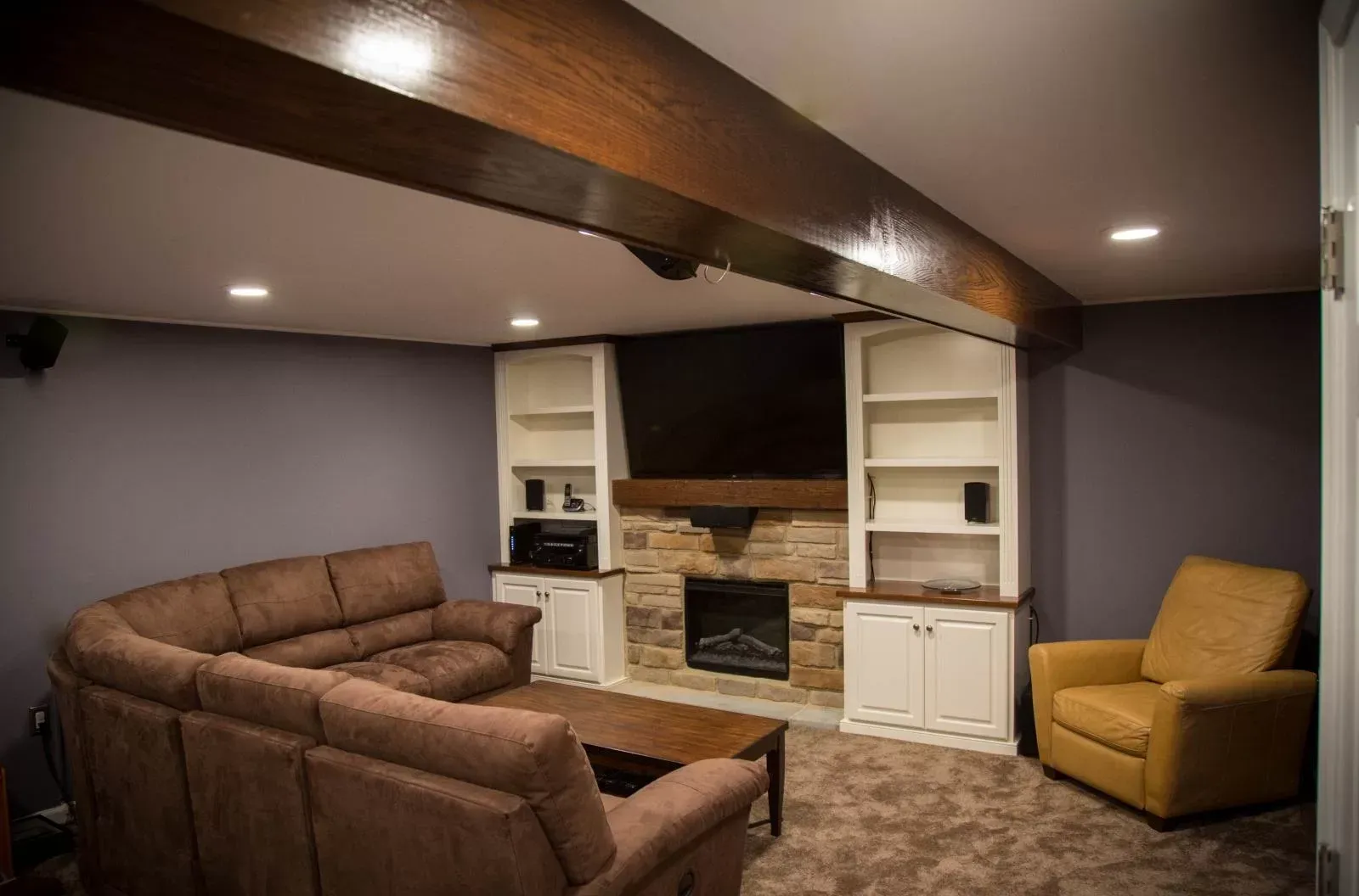 Cozy living room with a brown sectional, fireplace, built-in shelving, and a brown recliner against a purple wall.
