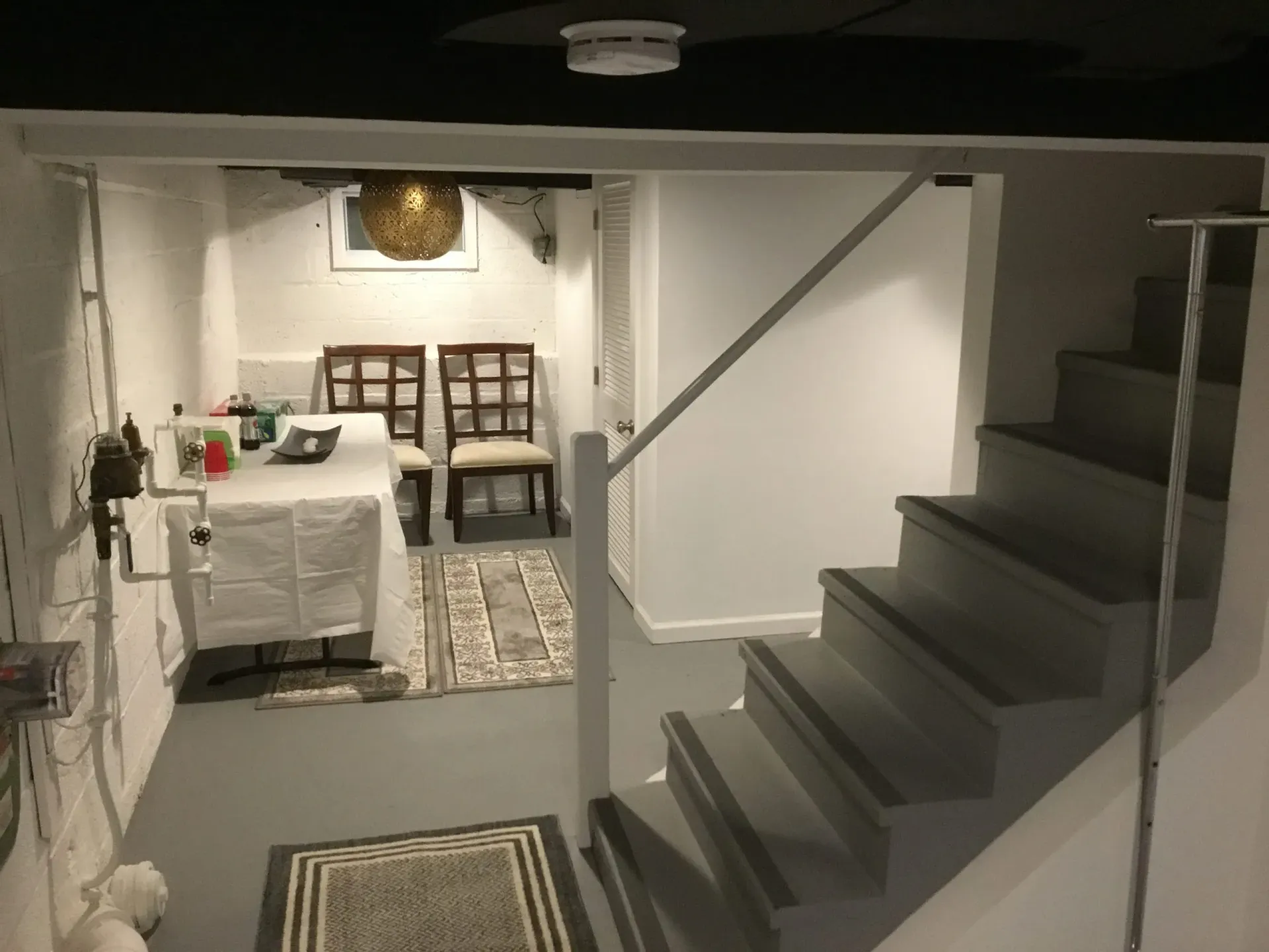 Basement with stairs, dining area, gray and white paint, and a rug.