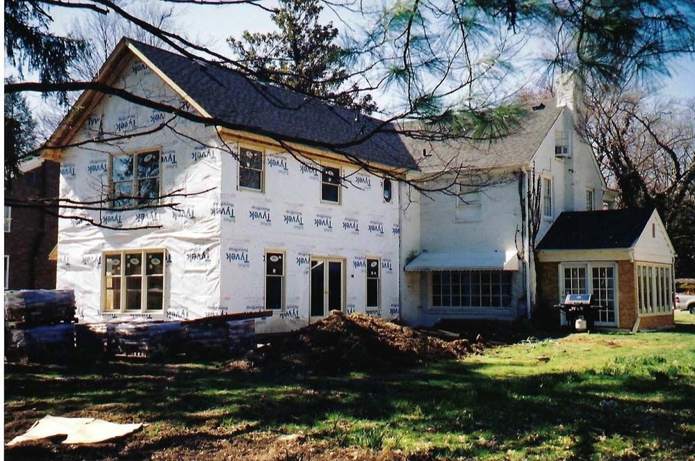 House under construction with exposed sheathing, windows, and new roof. Lawn and trees in yard.
