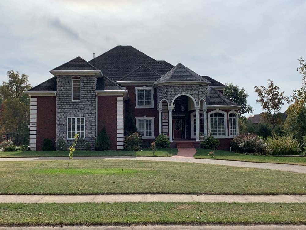 Large brick and stone house with dark roof and arched entrance on a grassy lawn.