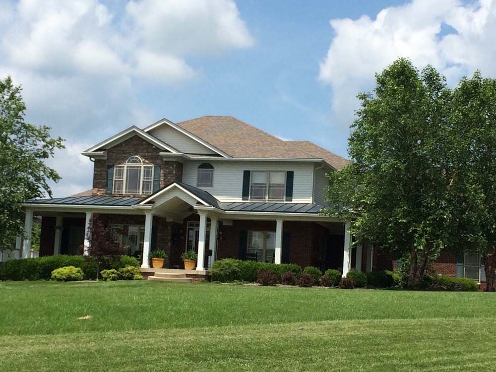 Two-story house with stone and brick exterior, porch, and a green lawn under a partly cloudy sky.