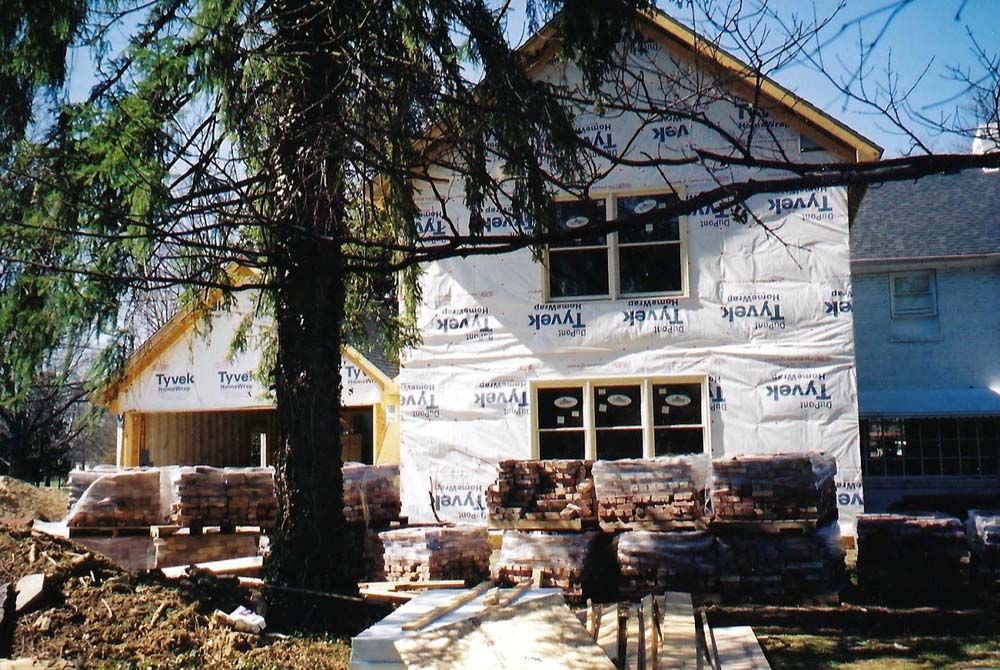 House under construction, exterior wrapped in Tyvek. Bricks stacked in front.