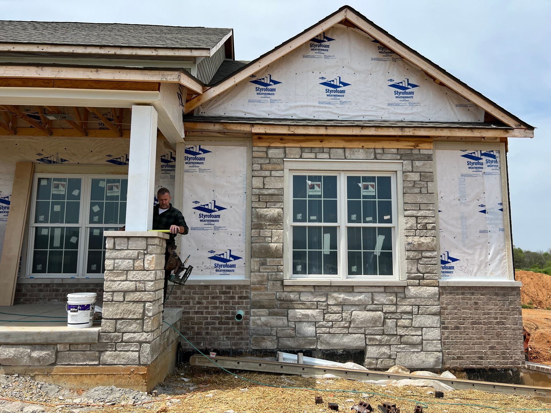 House under construction with stone exterior, windows, and a worker measuring.