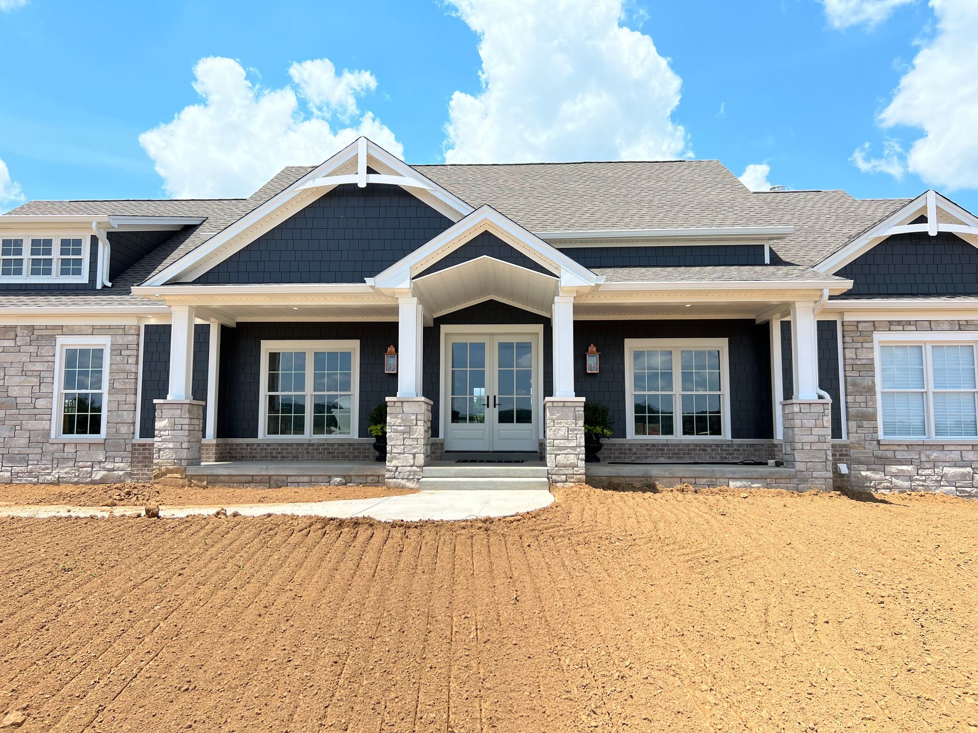 Blue and stone home with white trim and a blue sky.