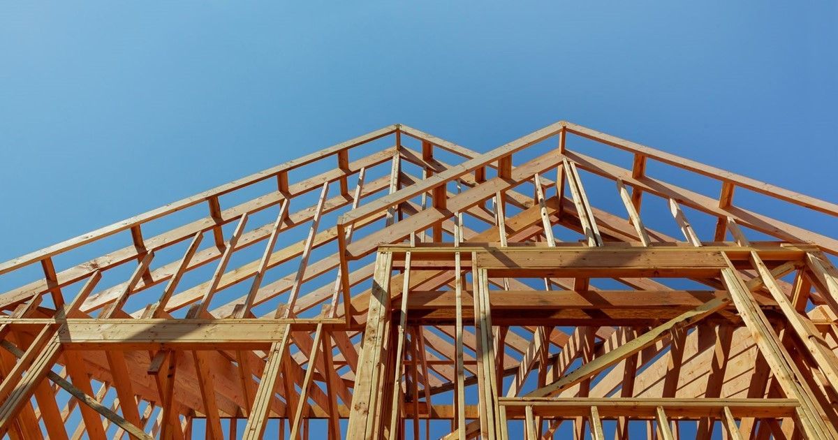 Wooden frame of a house under construction against a clear blue sky.