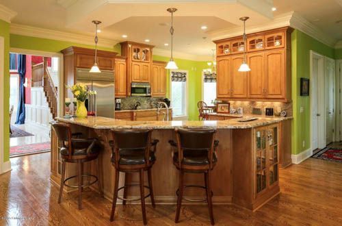 Kitchen with light-brown cabinets, granite countertops, and green walls. Bar stools at island.