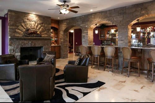 Luxurious living room with stone fireplace, bar, leather seating, zebra rug, and arched doorways.