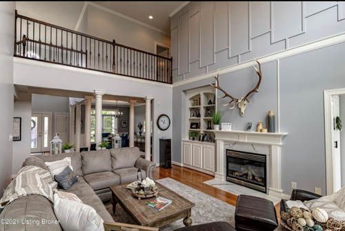 Living room with grey walls, fireplace, and balcony. Features a large sectional sofa and deer antlers.