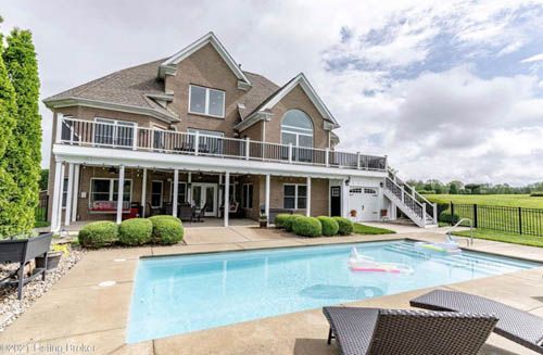 Large brick house with a pool, balcony, and green lawn on a cloudy day.