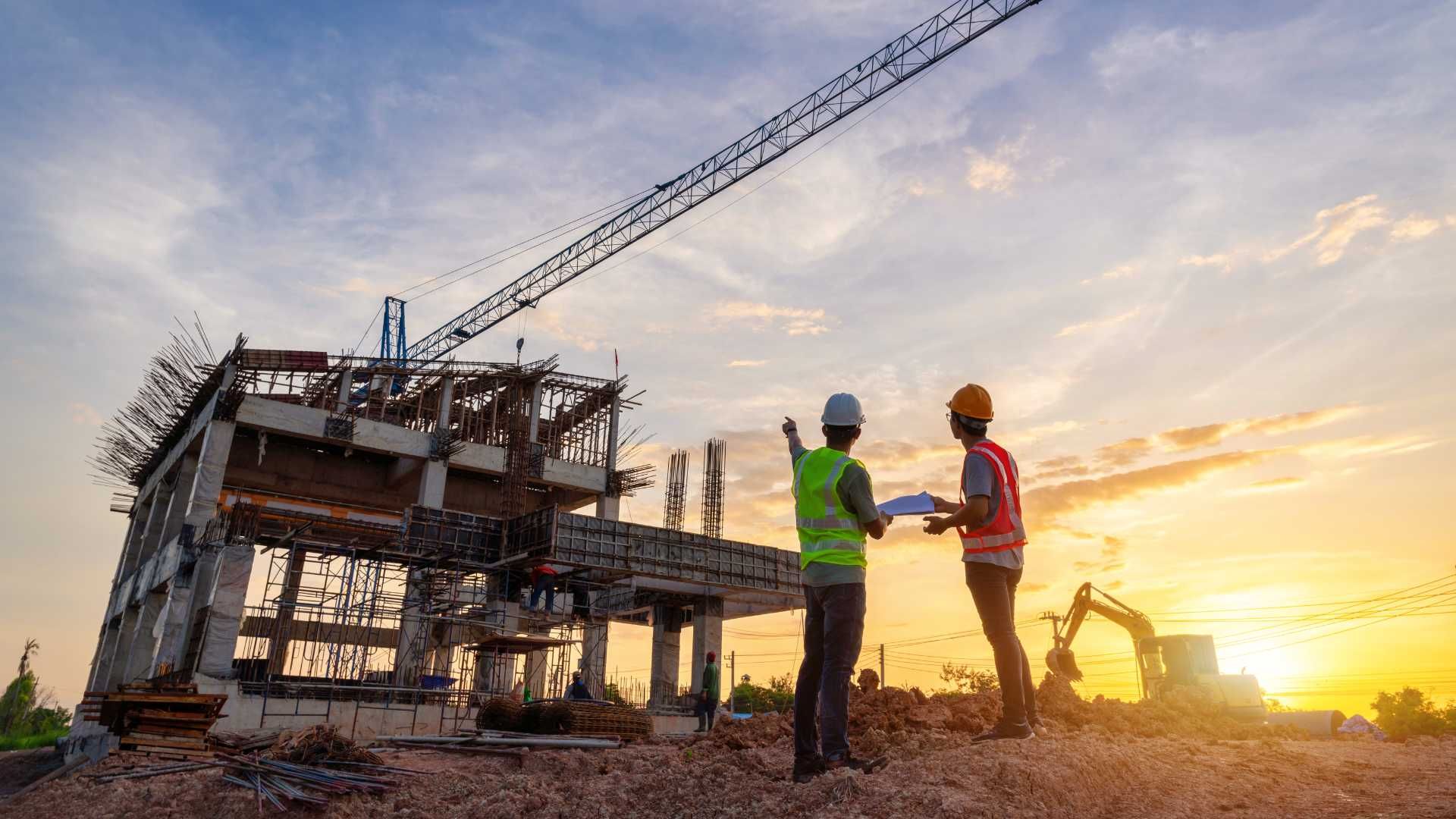 Two construction workers are standing in front of a building under construction.