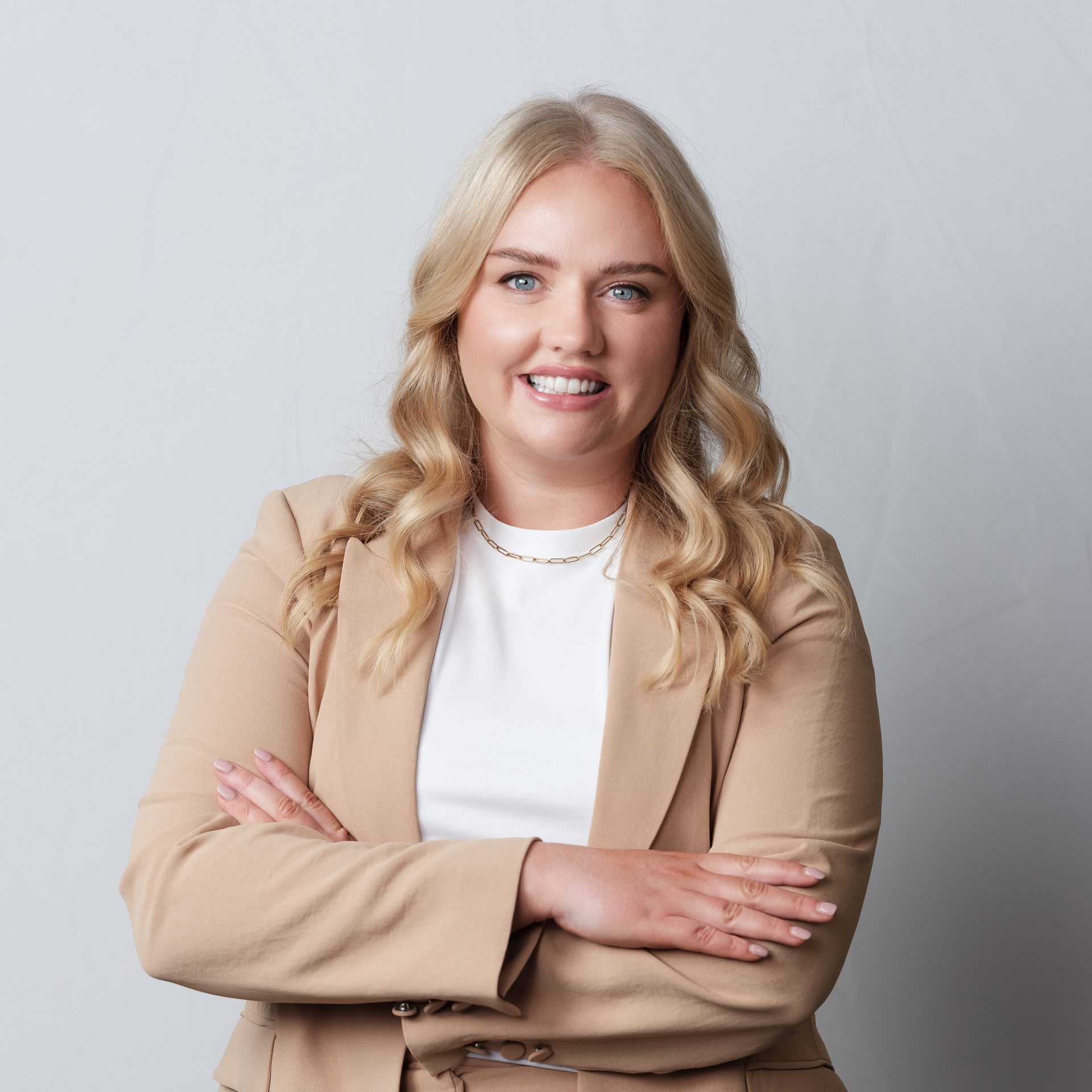 Woman with blonde hair wearing a tan blazer, arms crossed, smiling.