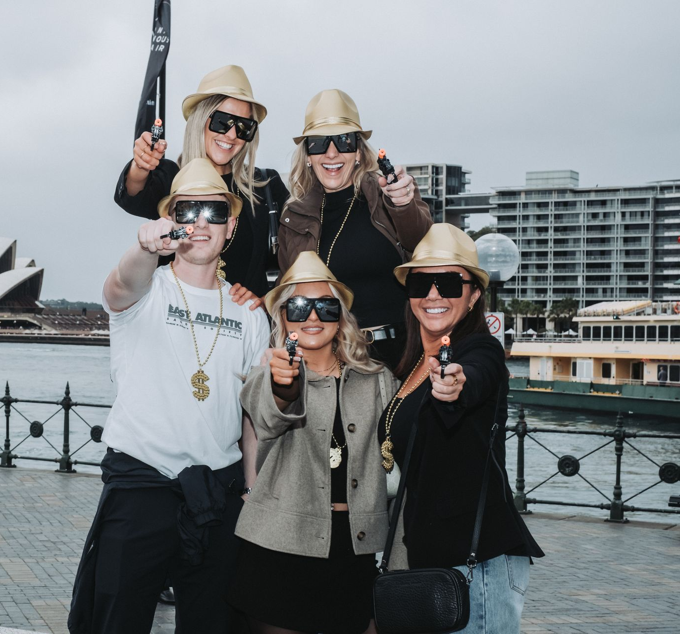 Five people posing with toy guns in front of the Sydney Opera House.