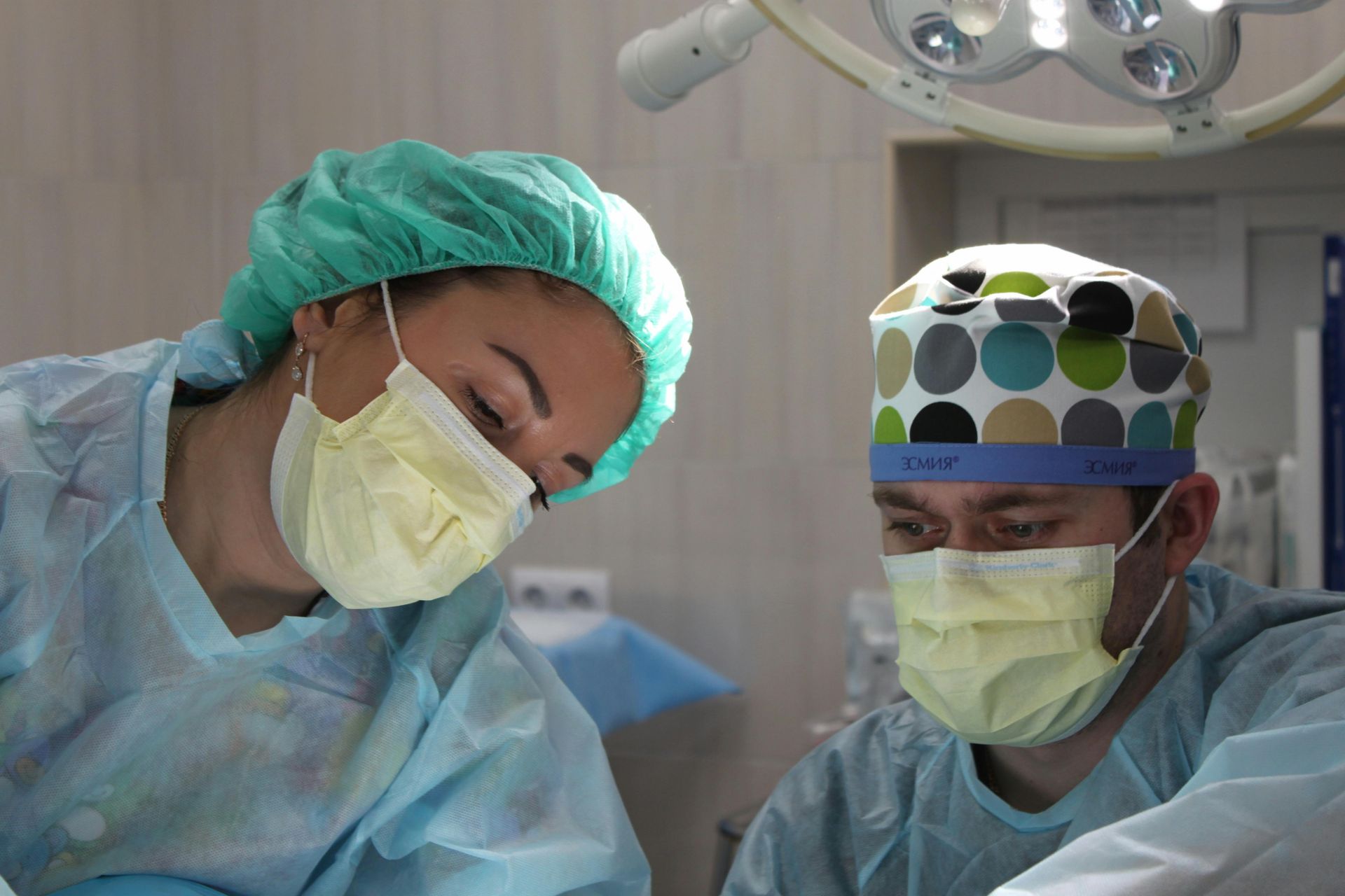 Two medical professionals in surgical attire, focused on a procedure under bright lights.