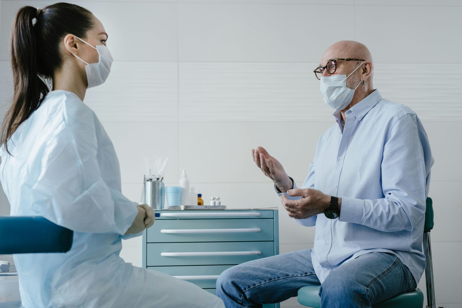 A healthcare worker and patient wearing masks talk in a medical setting.