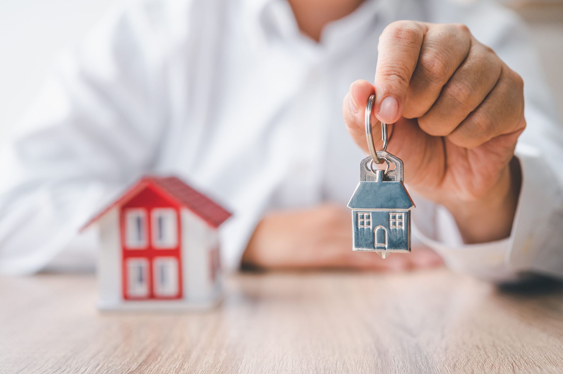 Hand holding a small house keychain beside a red model house on a table