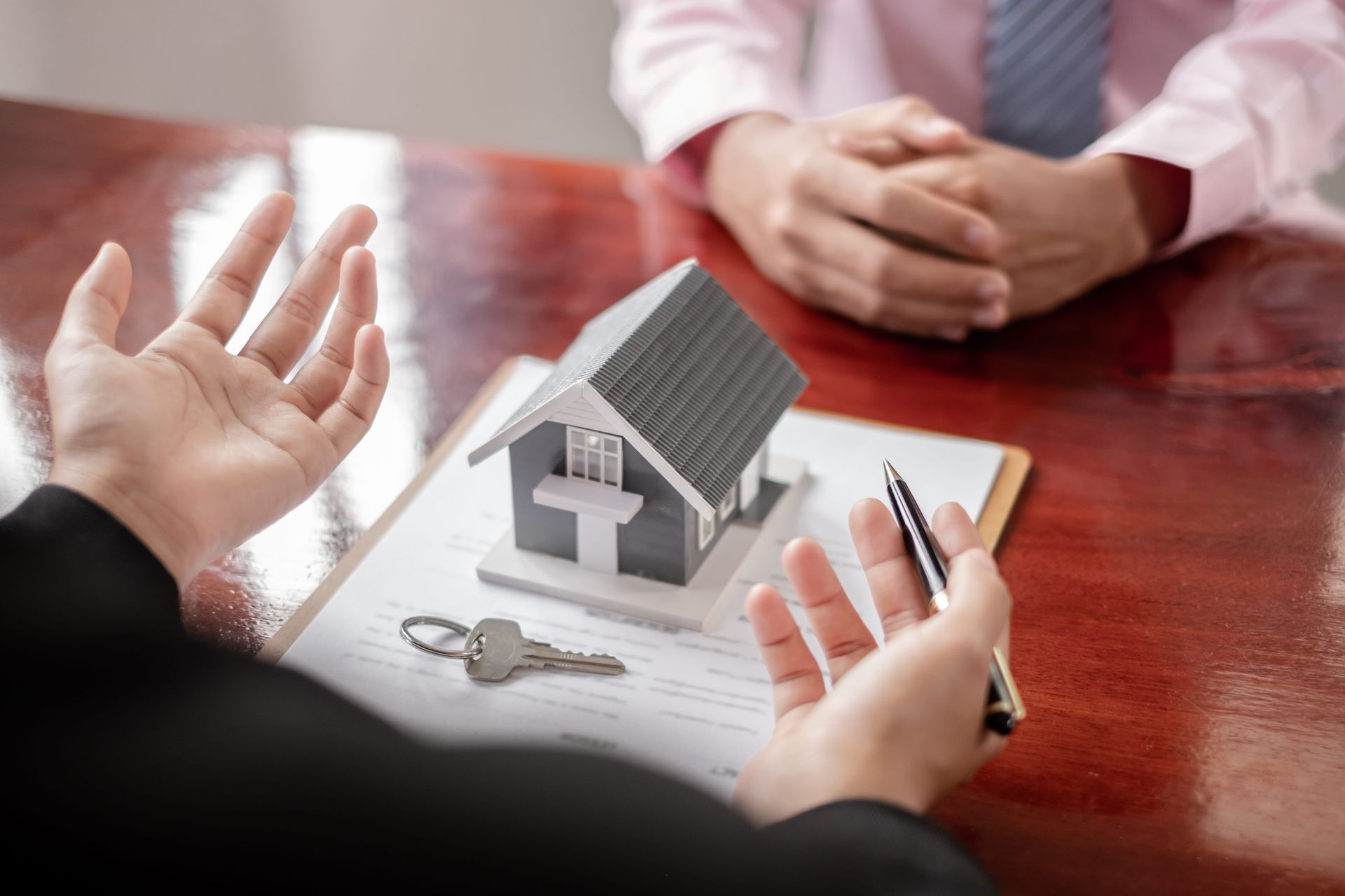 Hands discussing a house model and keys on a table during a real estate meeting