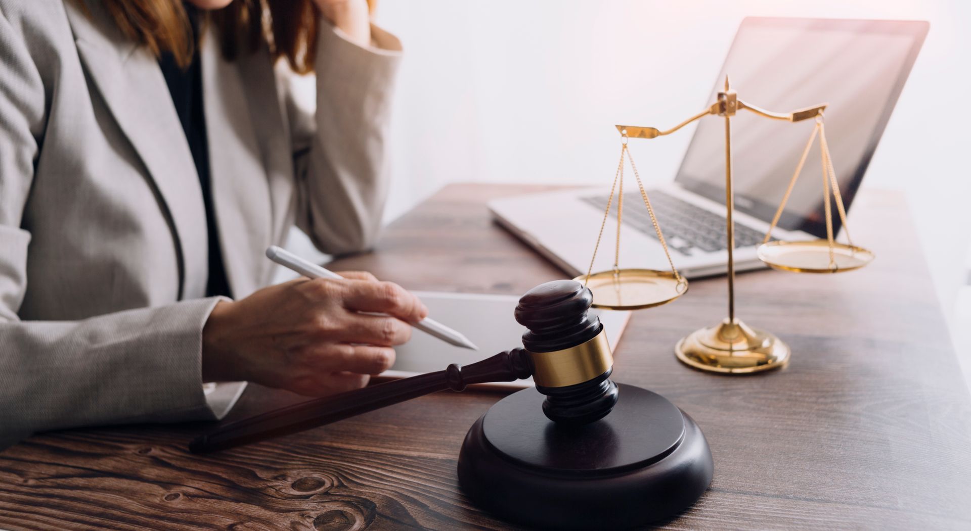 A person sitting at a desk with a gavel, scale of justice, and laptop.