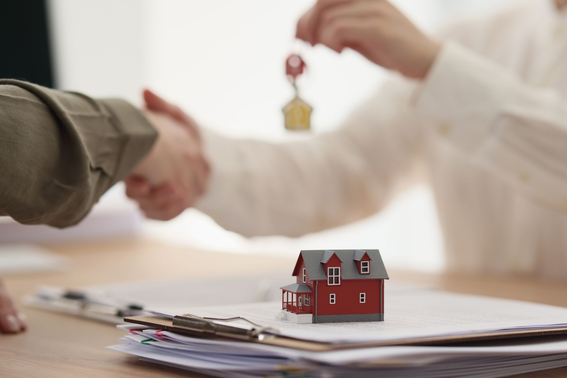 Real estate transaction: Handshake, keys, miniature house, paperwork on desk.