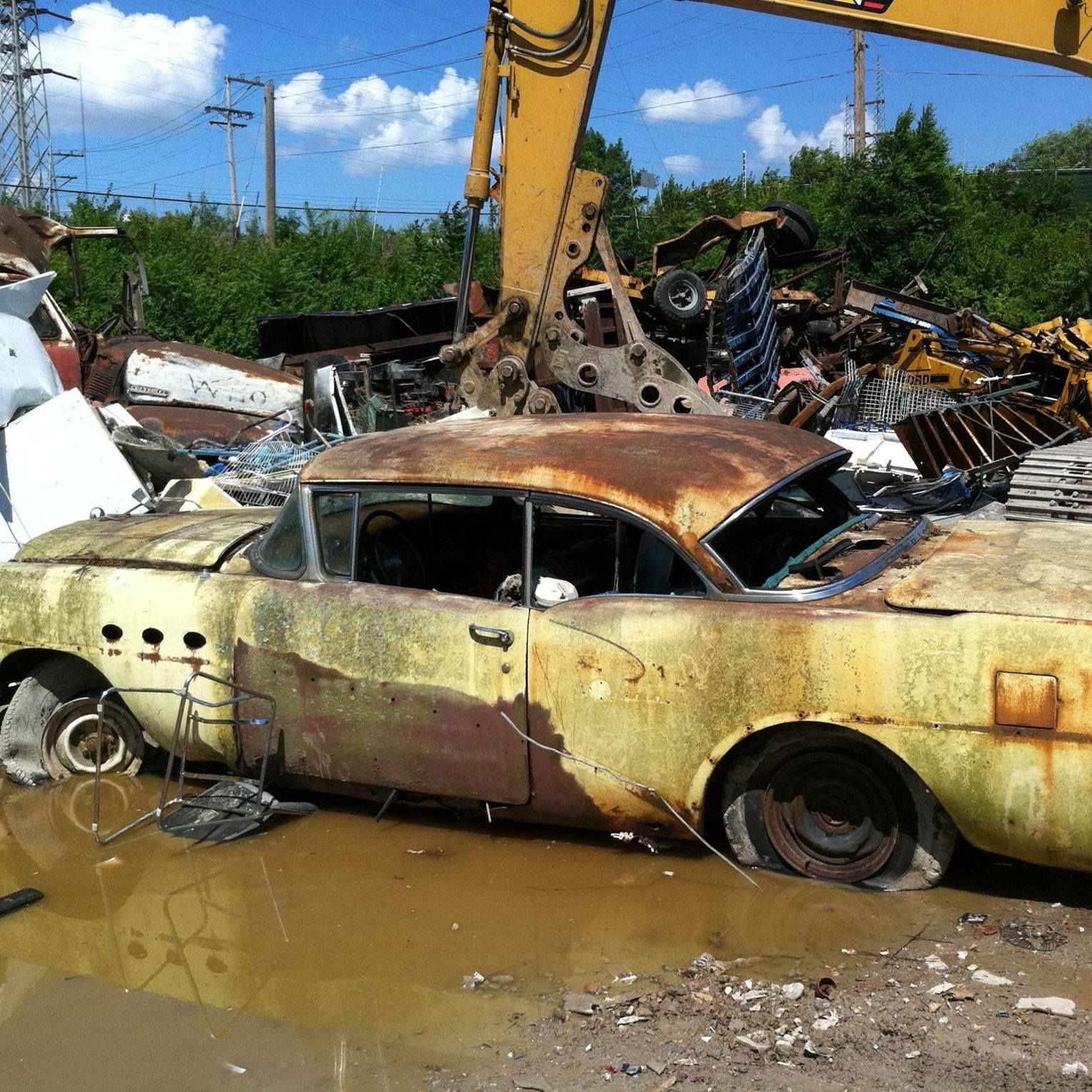 An old rusty car is sitting in a pile of scrap metal