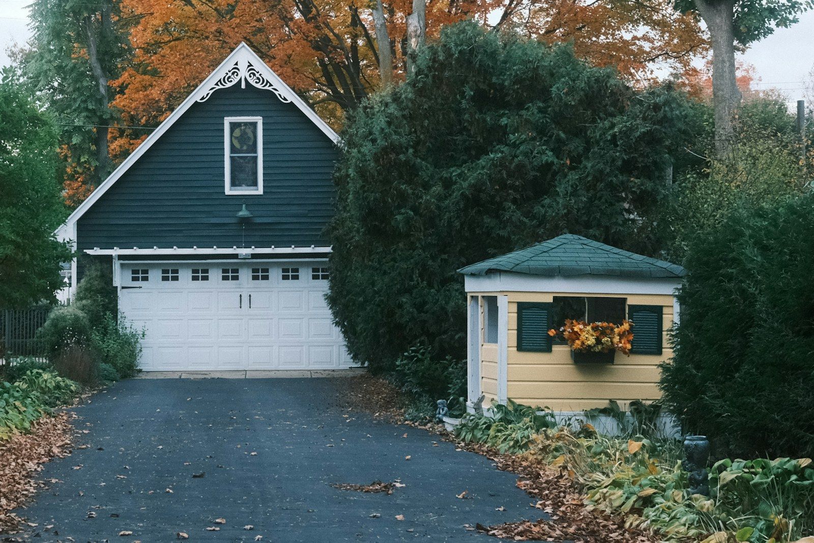 A white sectional garage door on a detached garage, with autumn leaves across the driveway