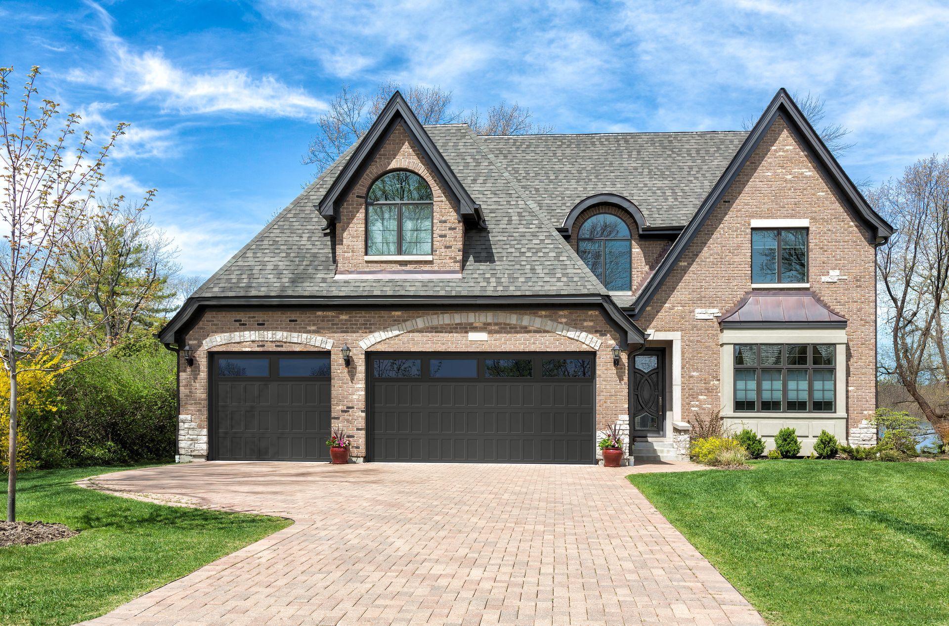Two black garage doors installed on a brick home with a paved driveway in Waynesboro, VA.