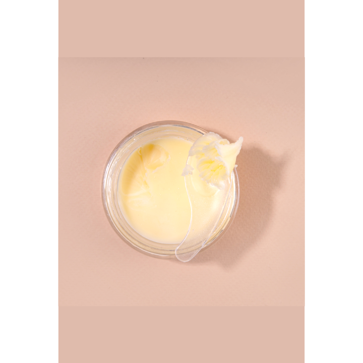 A close up of a jar of cream on a pink surface.