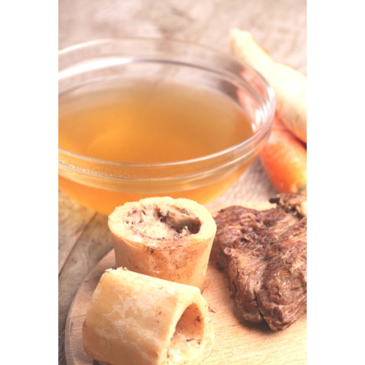 A bowl of broth next to some bones and meat