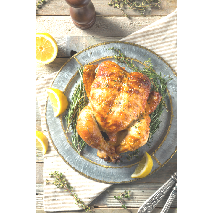 A roasted chicken on a plate with lemon slices and rosemary.