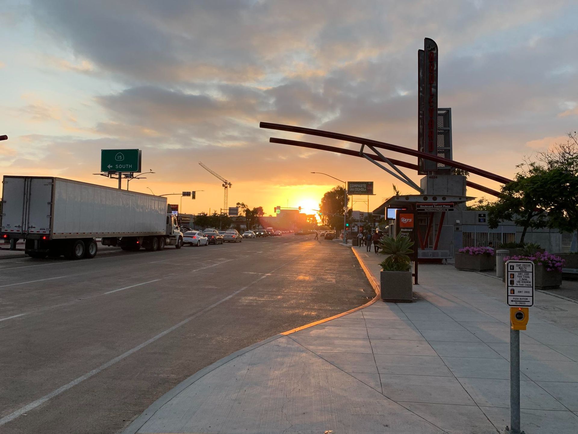 Sunset over a city street with trucks, sidewalk, and traffic lights near a modern building