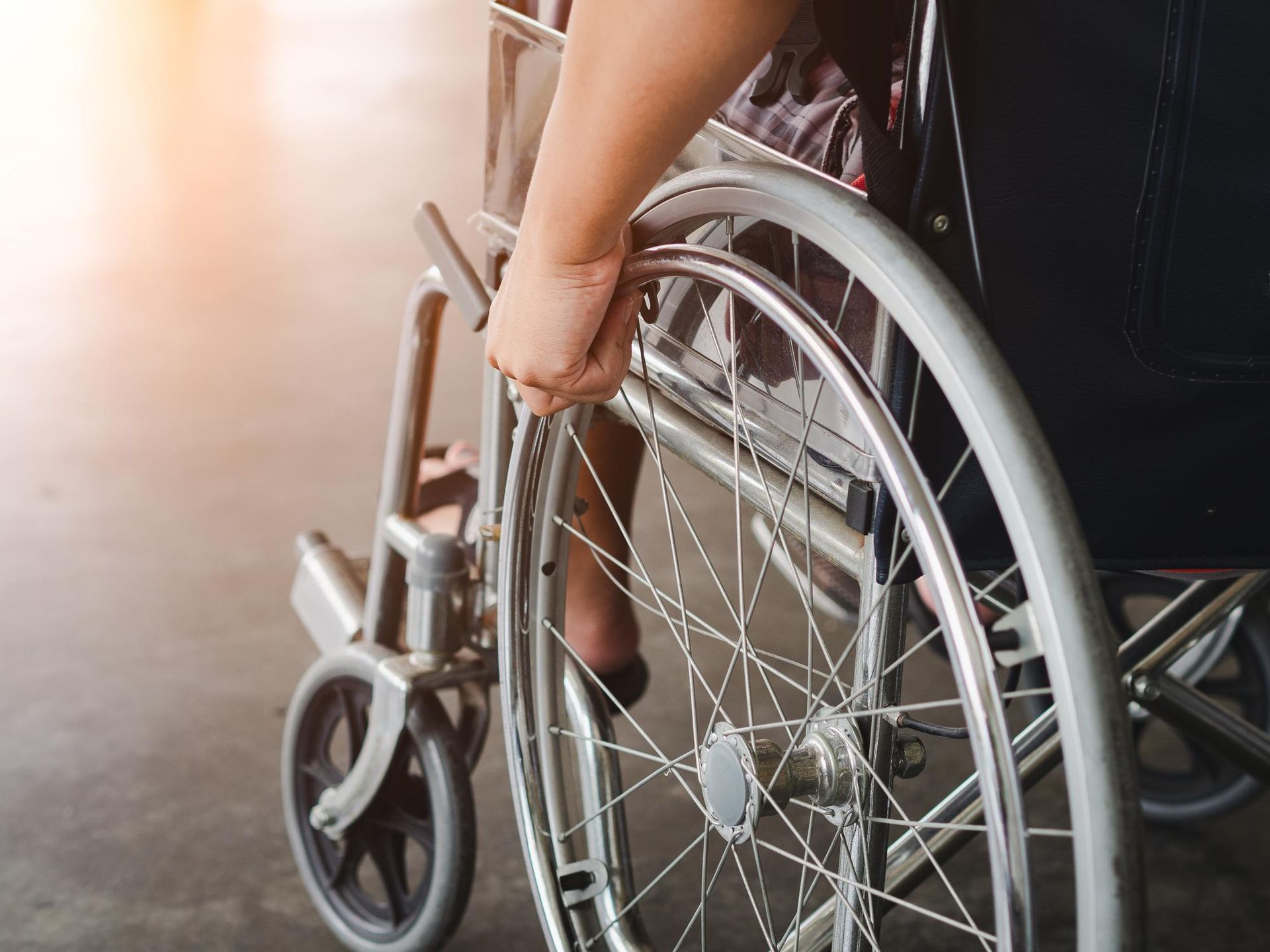 Person holding a wheelchair wheel indoors, with a small front caster visible.
