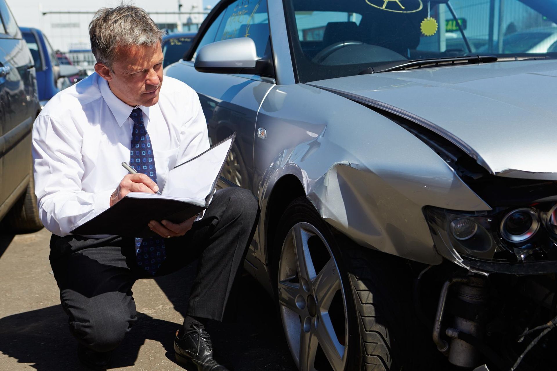 Insurance adjuster inspecting damage on a black car after a crash, taking notes beside the damaged front end