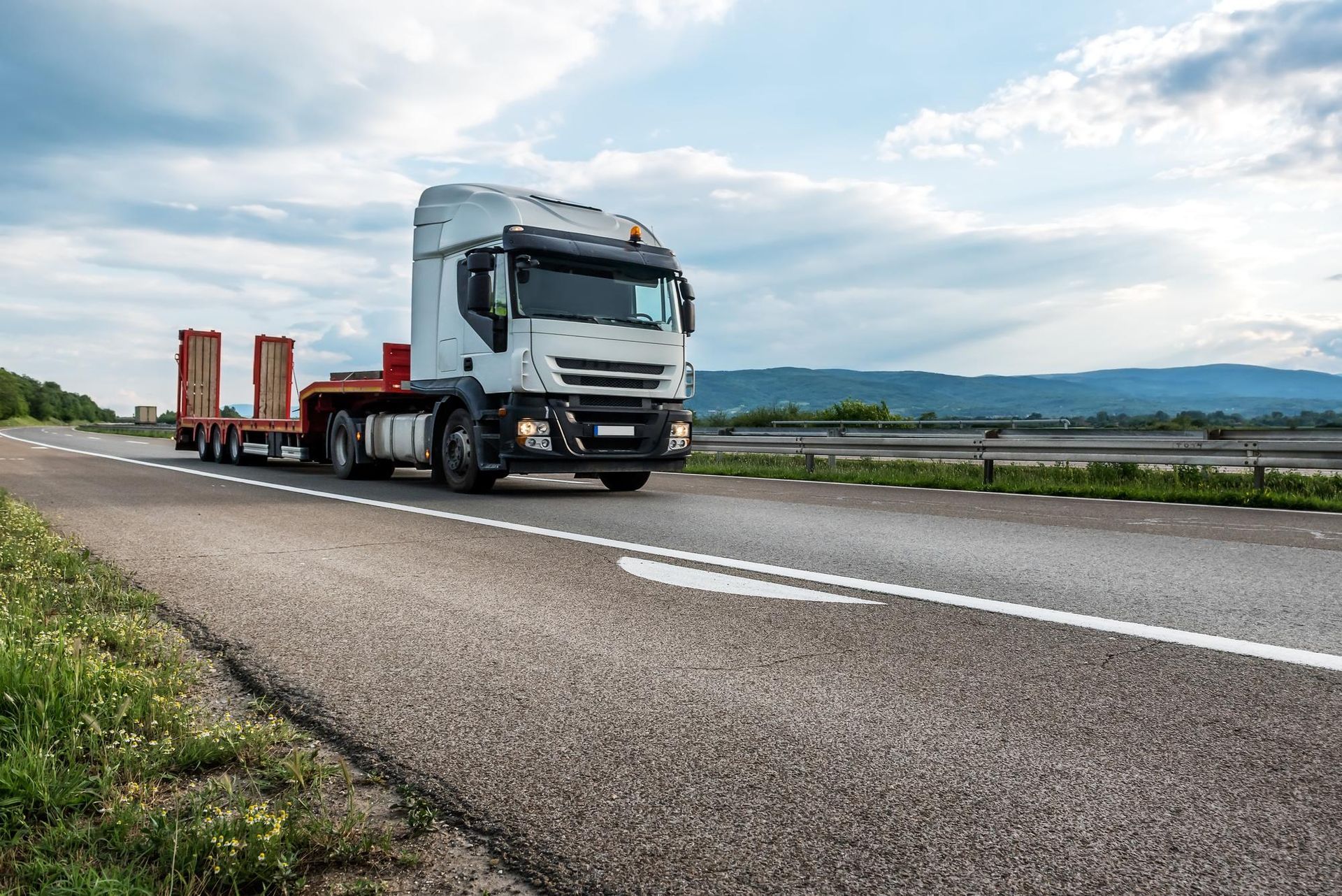 White cargo truck on a highway with a cloudy sky and mountains in the distance