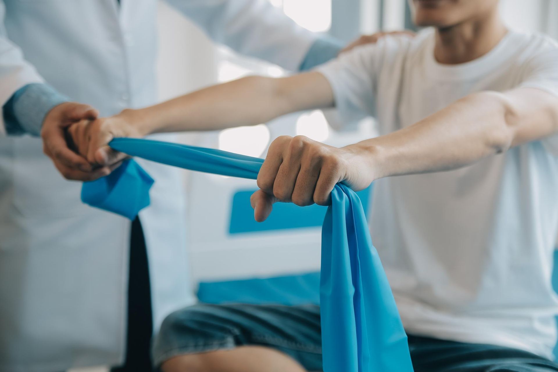 Two people stretching a blue resistance band during a workout