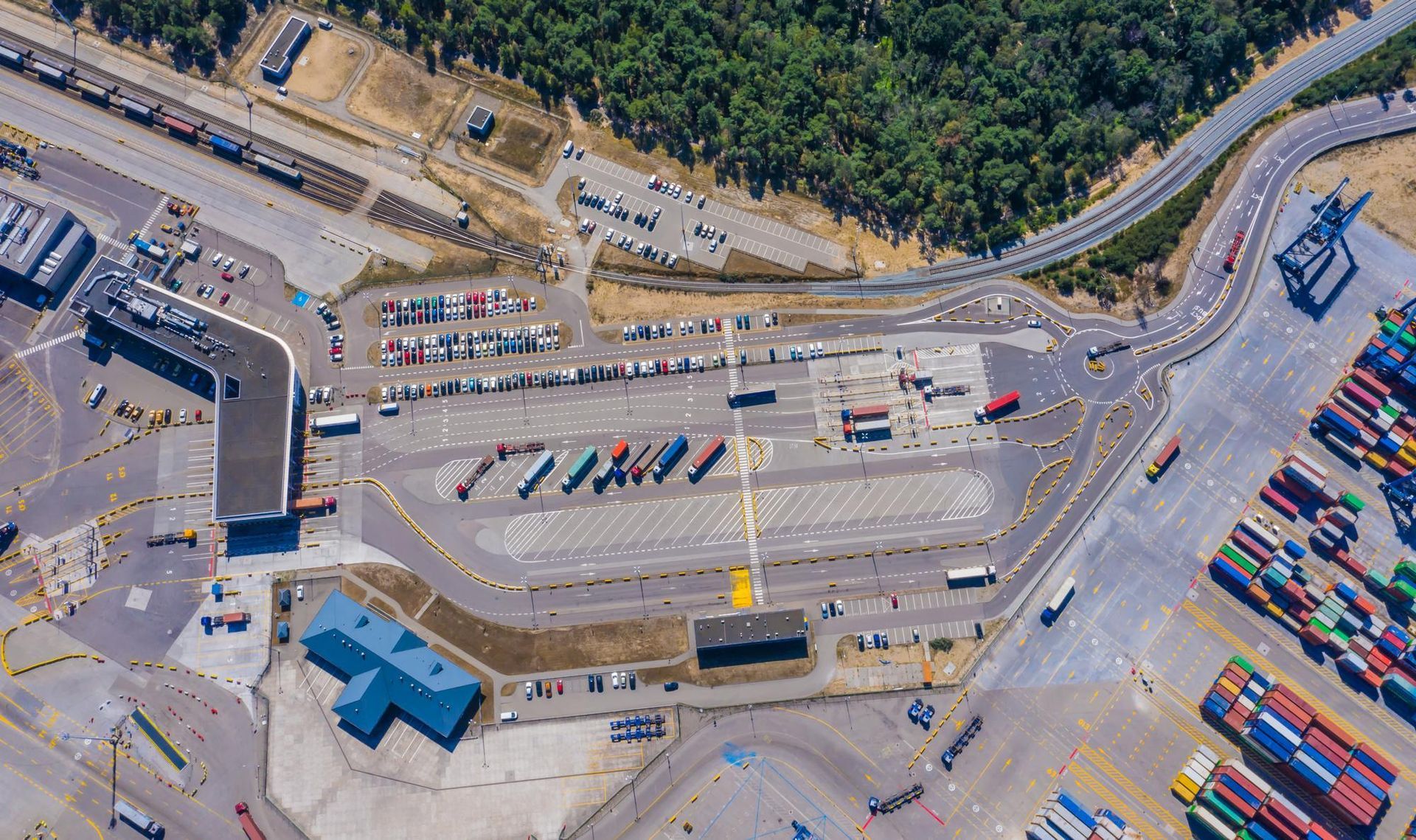 Aerial view of a busy port with trucks, shipping containers, and a large white ferry at the dock.