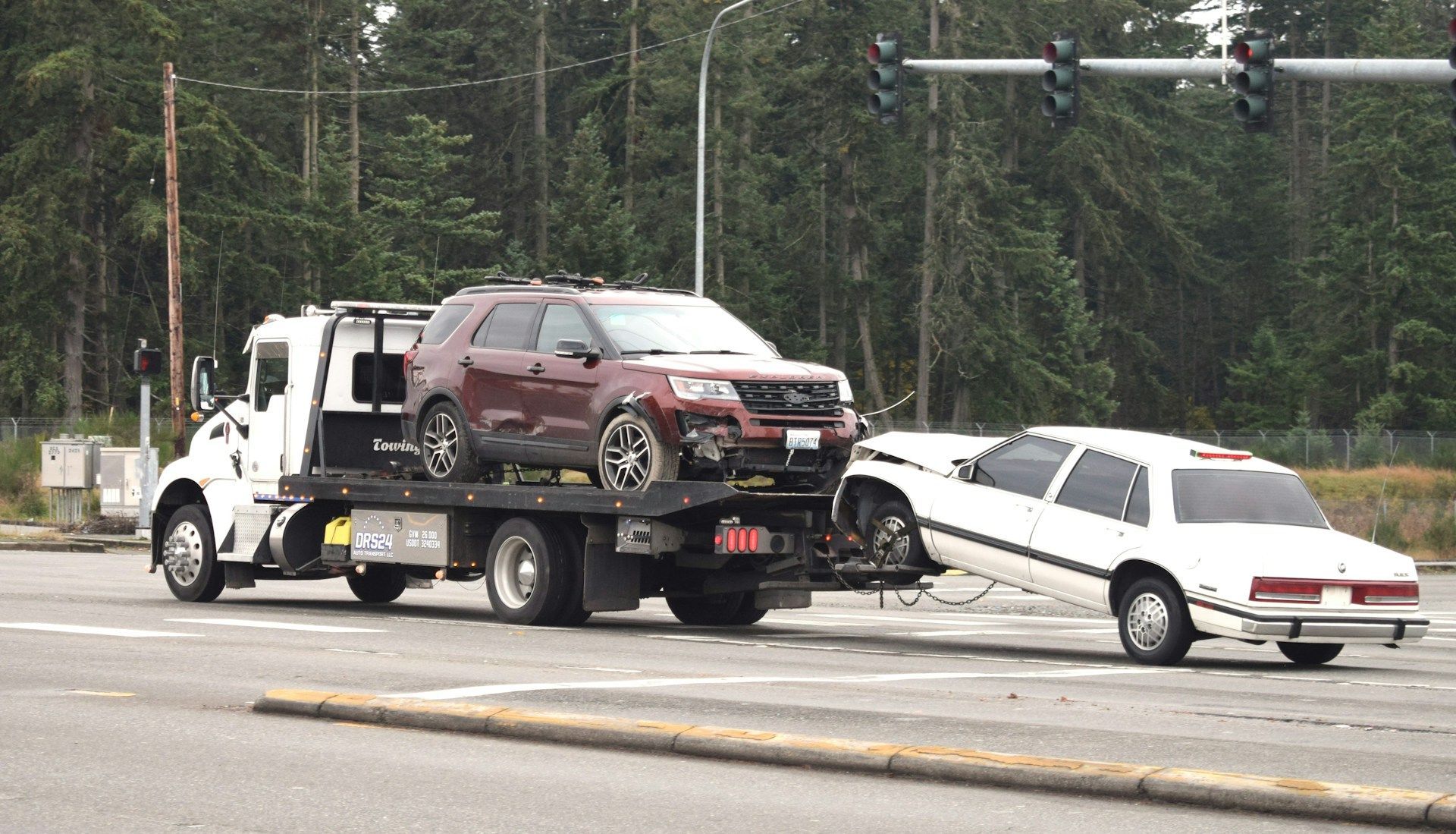 Tow truck hauling a red SUV and a white sedan after a roadside crash