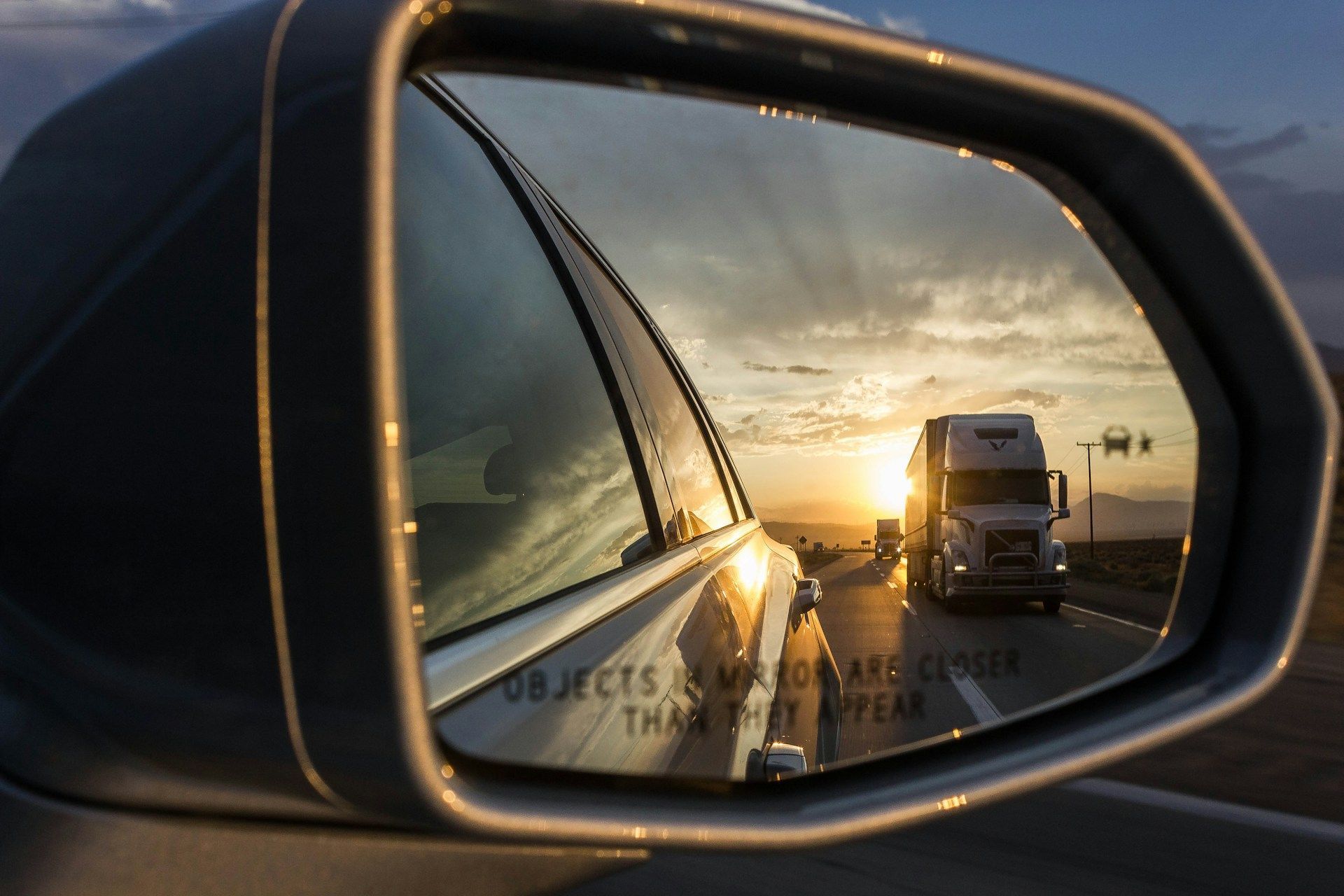 Side mirror reflecting a truck on a highway at sunset